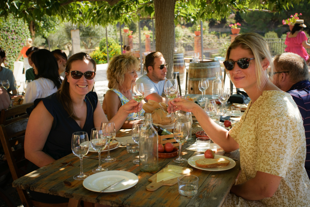 Friends smiling and enjoying a glass of white wine on the table, during their wine tasting activity at the winery after the vineyard tour